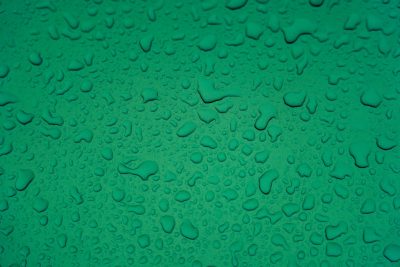 A flat, uniform background of water droplets on green surface. The drops should be arranged in an random pattern with no clear patterns or shapes. They must cover the entire canvas and appear to have just fallen onto it from above. Each drop is clearly visible against the smooth texture of the greenshade background. There's space at top for text or other elements. --ar 128:85