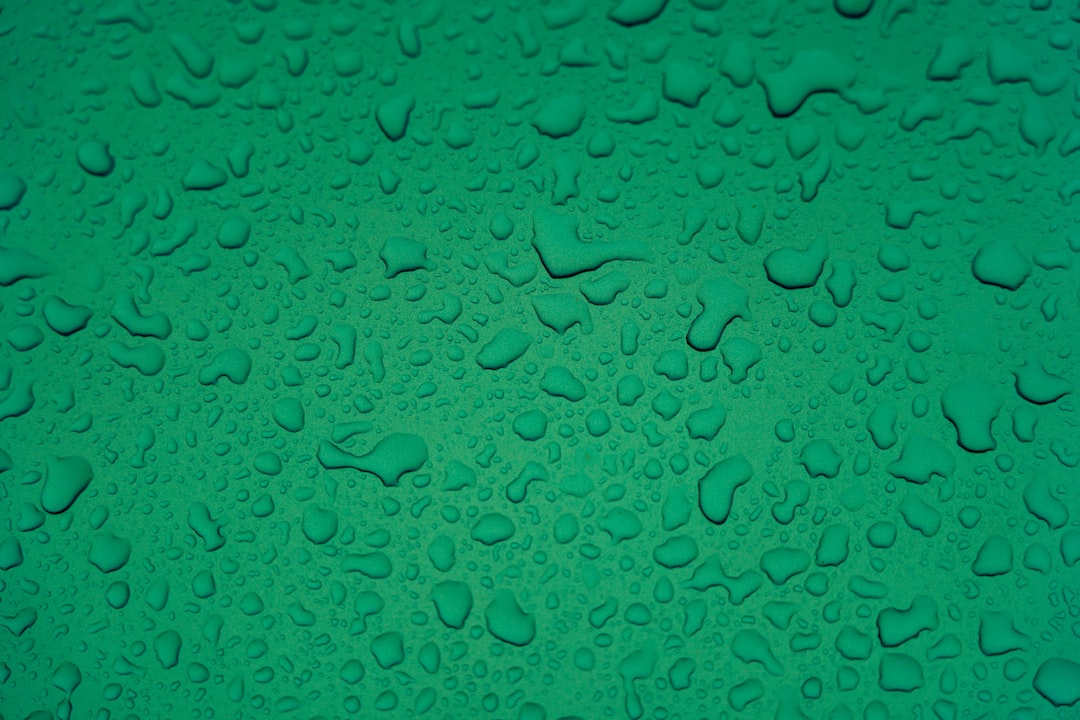 A flat, uniform background of water droplets on green surface. The drops should be arranged in an random pattern with no clear patterns or shapes. They must cover the entire canvas and appear to have just fallen onto it from above. Each drop is clearly visible against the smooth texture of the greenshade background. There’s space at top for text or other elements. –ar 128:85