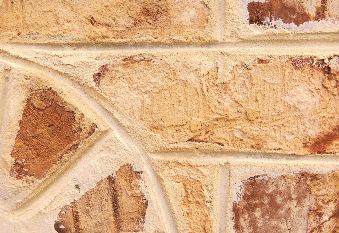 Closeup of an old, weathered beige stone wall with intricate details and textures. The texture is very detailed, showing the different shapes and sizes of bricks, as well as signs of wear and tear such as chipped edges or rust spots. This closeup shot captures the beauty in imperfection and history that each brick holds within its surface. The background should be plain to highlight the detail on the wall itself. –ar 16:11