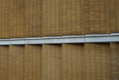 The exterior wall of the building is made up entirely of horizontal lines of brown bricks, with gray metal frames between them. The background has a simple and clean style, with no other elements in it. This brickwork creates an interesting texture on its surface. The style is reminiscent of modern architecture, depicted in real photography. --ar 64:43