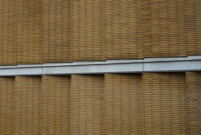 A close up of the wall, showing an industrial building facade made from brown brick with horizontal bands and a grey steel beam on top. Simple background, architectural photography, high resolution, high quality in the style of simple background.