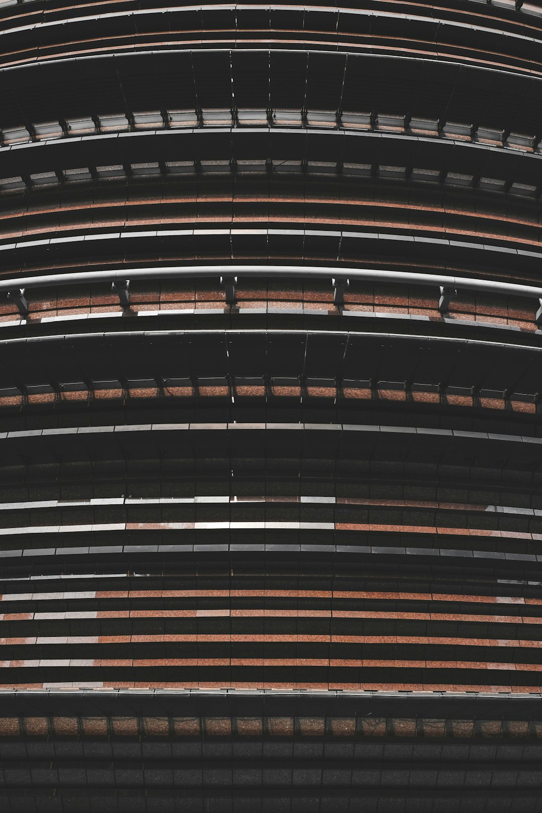 A photo of the exterior wall texture of an ovalshaped stadium, featuring horizontal stripes in shades of black and brown. The image captures the unique architecture with its curved lines and patterned details. This topdown view highlights how these strips come together to form the overall structure of the building. Shot by Nikon D850 with high resolution, cinematic lighting –ar 85:128