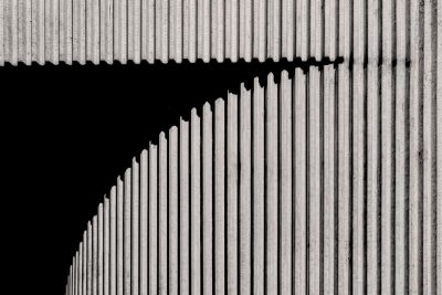 Black and white photograph of an industrial building wall with vertical lines, creating sharp shadows that highlight the texture and form of concrete. The background is dark to accentuate the architectural details. This style evokes a sense of modernity in urban architecture. --ar 128:85