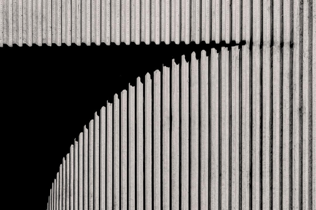 Black and white photograph of an industrial building wall with vertical lines, creating sharp shadows that highlight the texture and form of concrete. The background is dark to accentuate the architectural details. This style evokes a sense of modernity in urban architecture. –ar 128:85