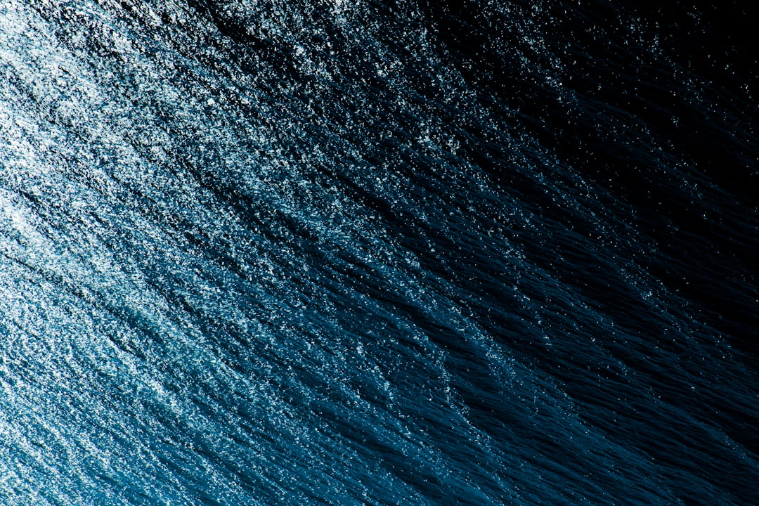 A closeup of the dark blue sea, with gentle ripples and light reflections on its surface. The camera captures an overhead view of the entire scene from above. The composition emphasizes the beauty of the water’s texture against a black background. High resolution photography captures the photo realistically. Shot in the style of Hasselblad H6D400c Mf XCD lens. –ar 128:85