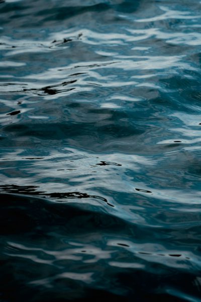 A closeup of the dark blue water surface, with ripples and reflections in it. The background is blurred and dark, creating an atmosphere full of mystery and tranquility. Soft lighting illuminates the calm waves on the sea level, adding depth to the scene. High definition photography style, highlighting details and textures.,,in --ar 85:128