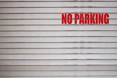 A photo of the text "NO PARKING" written in red on a white metal garage door, in a minimalistic and clean style, with high resolution. --ar 128:85