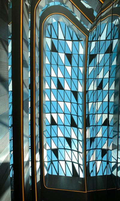 Blue and black, art deco style pattern on a glass curtain wall with the sun shining through in a Dubai tower interior designed in the style of [Frank Gehry](https://goo.gl/search?artist%20Frank%20Gehry) with gothic accents using LED lights to cast shadows of triangular shapes onto the walls. --ar 19:32