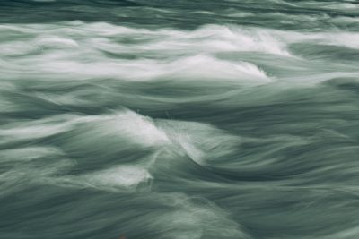 Abstract view of the rapids on Napoleon's river, featuring dynamic water patterns and soft green hues. The camera focuses in closeup to capture details like ripples or splashes against a blurred background. This composition emphasizes the energy and movement associated with powerful water, suitable for creative use in various applications. The style emphasizes closeup details of water movement against a blurred background, capturing the energy of rapids in soft green hues. --ar 128:85