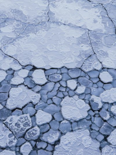 A closeup aerial view of cracked ice on the surface, with delicate patterns and textures in shades of blue. The scene is set against an icy background, capturing the beauty and texture of frozen water. High resolution photography, detailed in the style of natural light, sharp focus, stock photo. --ar 3:4