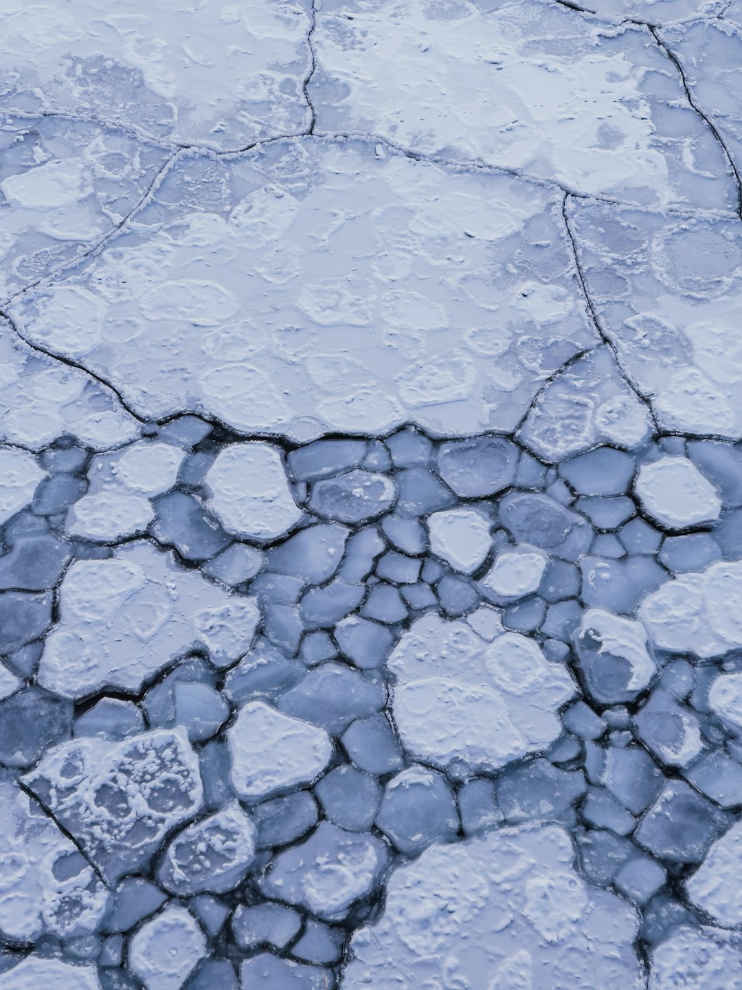 A closeup aerial view of cracked ice on the surface, with delicate patterns and textures in shades of blue. The scene is set against an icy background, capturing the beauty and texture of frozen water. High resolution photography, detailed in the style of natural light, sharp focus, stock photo. –ar 3:4