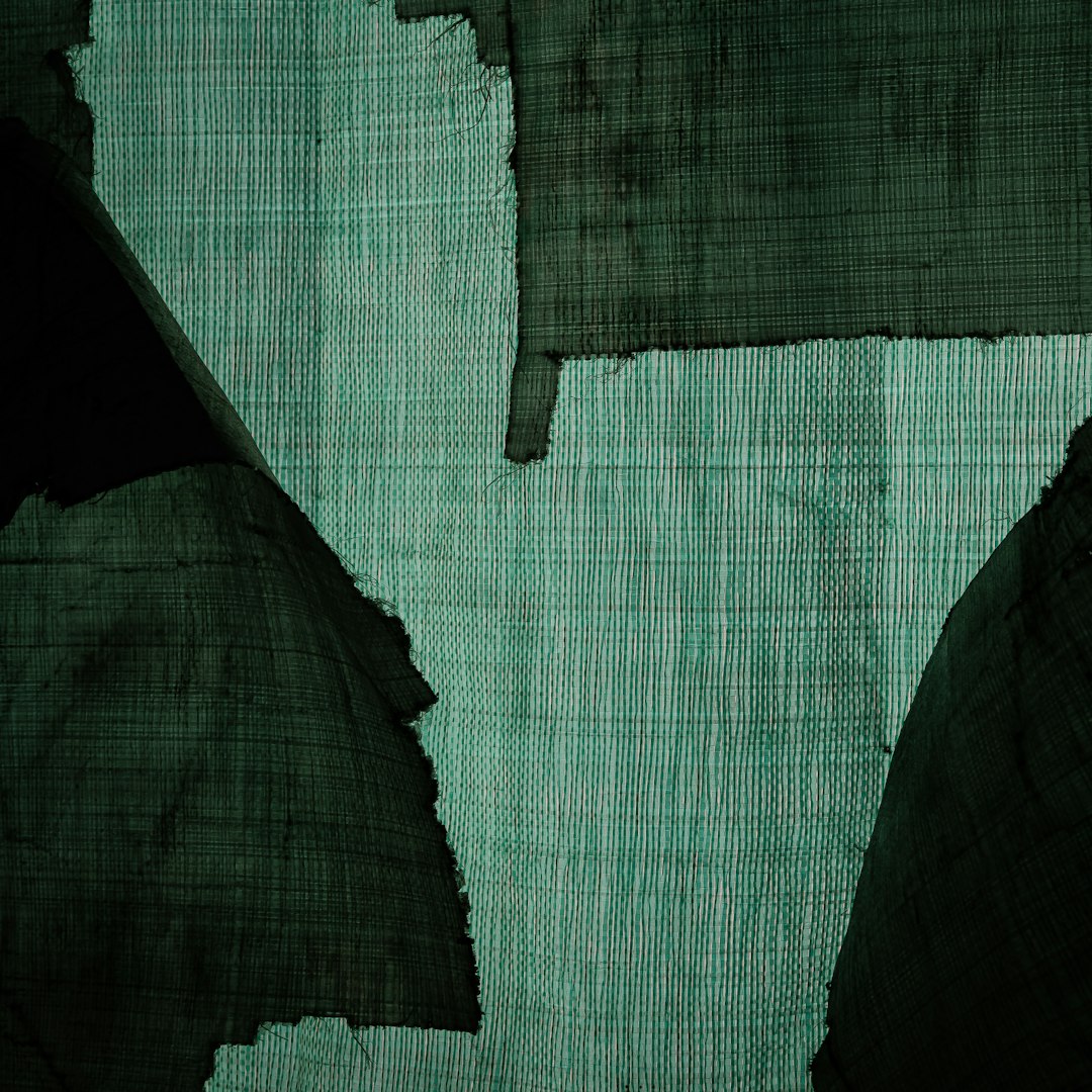 green woven fabric, flat surface, cut into pieces and torn to reveal the canvas underneath, dark green background, close up