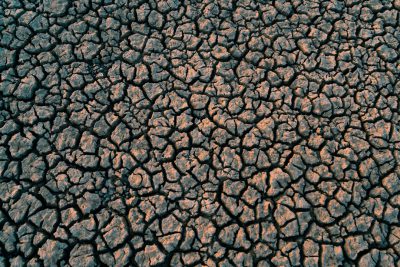 A top-down view of cracked earth, symbolizing the effect on soil under intense heat and dust conditions. The cracks represent dryness in nature, emphasizing how climate change can have an impact on plant life. --ar 128:85