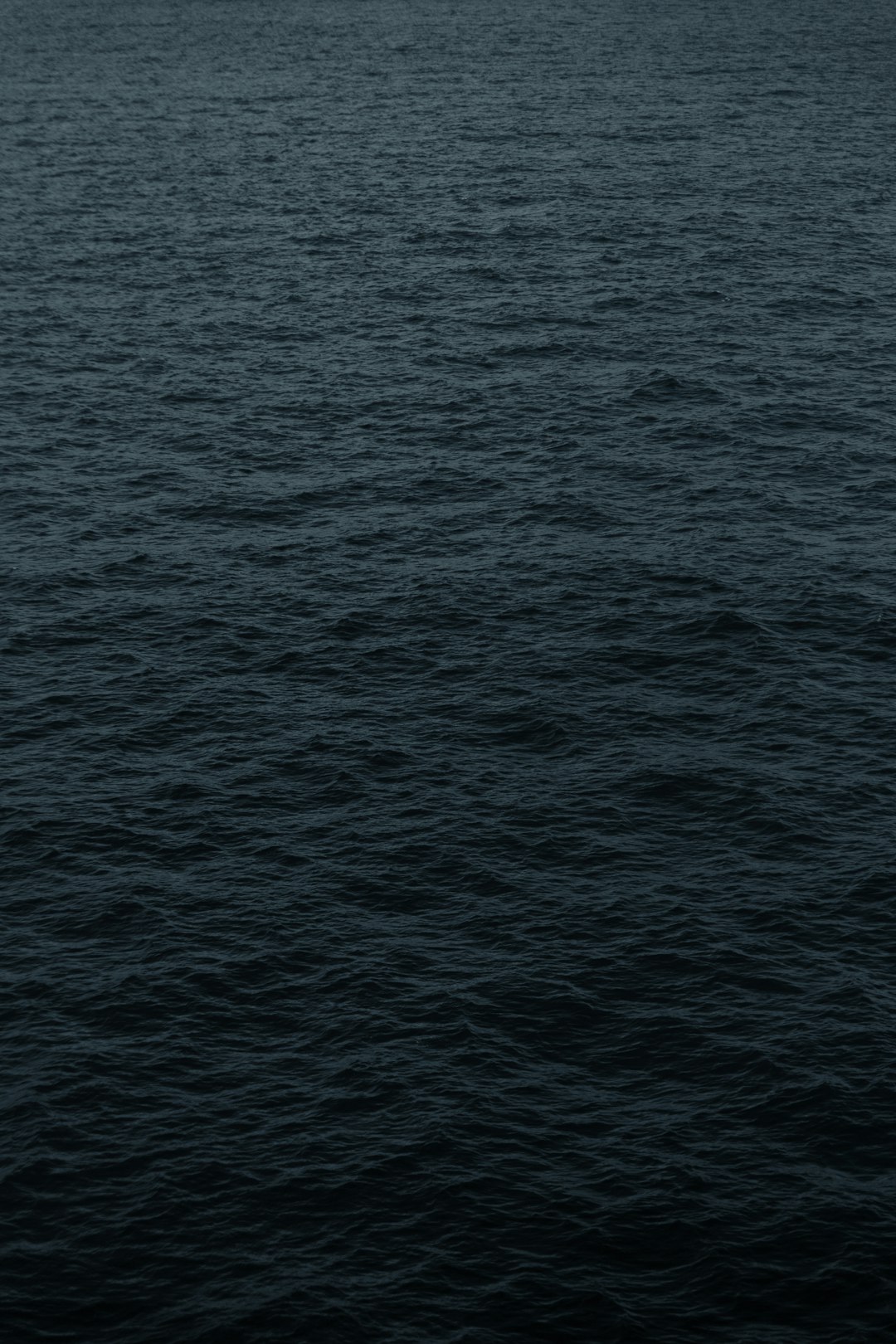 Dark blue water with a flat, dark gray background and no waves on the surface of the sea in a minimalist style with a simple background. A high resolution, hyperrealistic aerial shot in the style of reallife photography with detail from a top view as a professional photograph. –ar 85:128