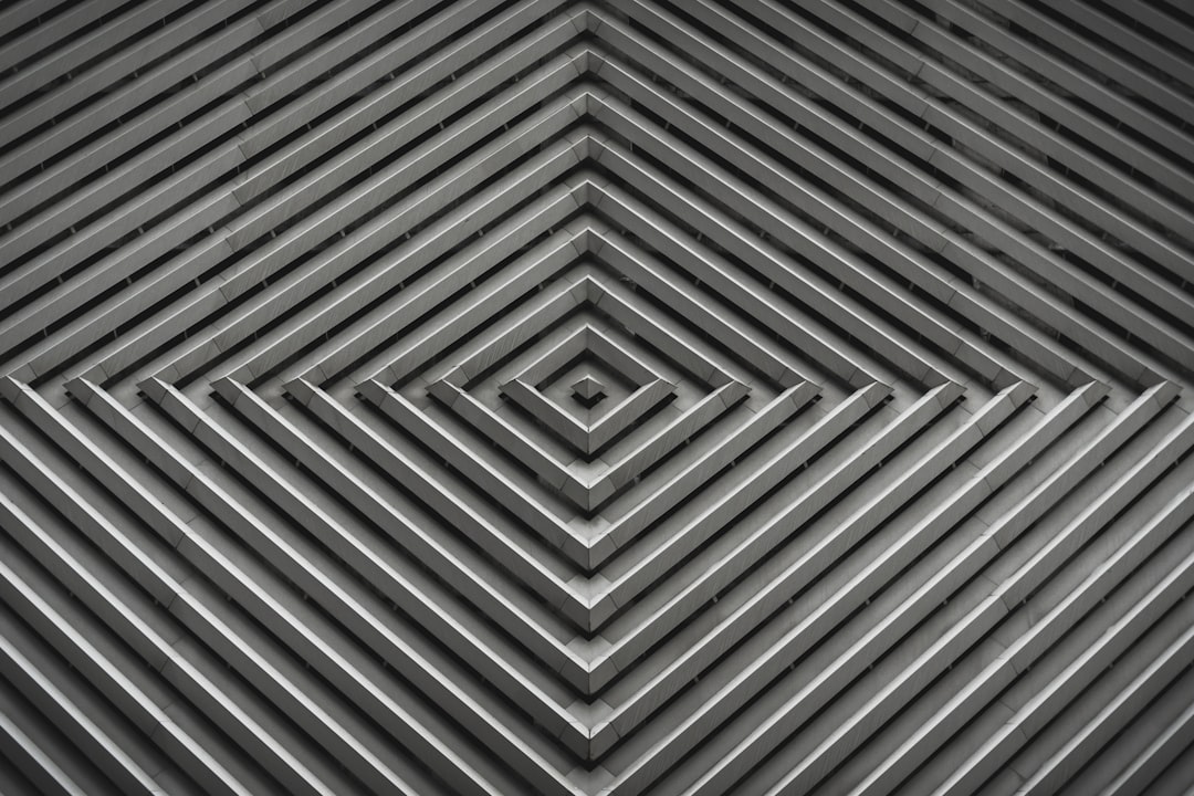 A black and white geometric pattern with lines that form squares, triangles or spirals. The background is made of gray metal and has a symmetrical design in the style of modern art. –ar 128:85