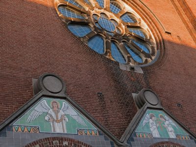 a close up of the side wall and roof line with stained glass angel images on it, and large round window in red brick church , small arches above windows, art deco style, architectural photography --ar 4:3