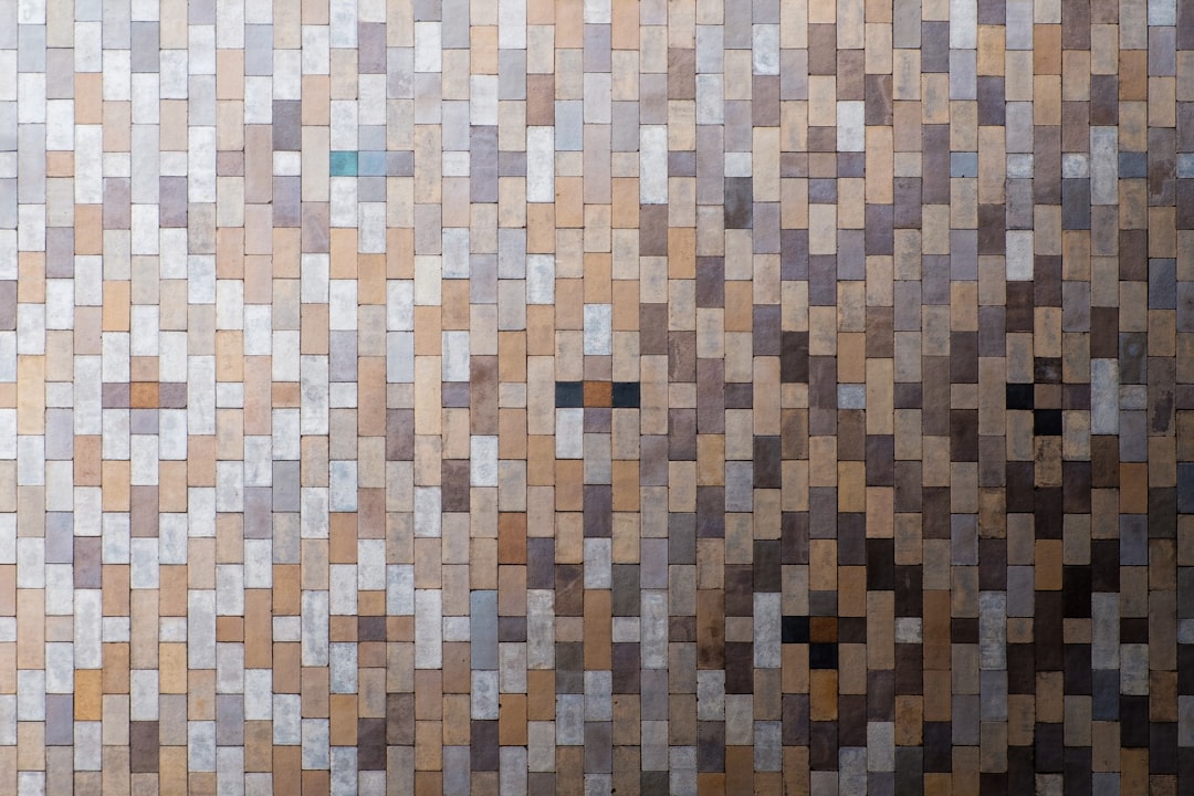 A wall made of square tiles in different shades of brown, grey and silver. The tile pattern is seamless and uniform throughout the whole background. –ar 128:85