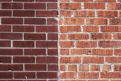 A red brick wall with half painted in dark brown color, contrasting the other side. The left part of it is painted and has a smooth texture while the right one shows the natural red brick pattern. It is a closeup photo focused on the texture and color contrast between the two parts. --ar 128:85