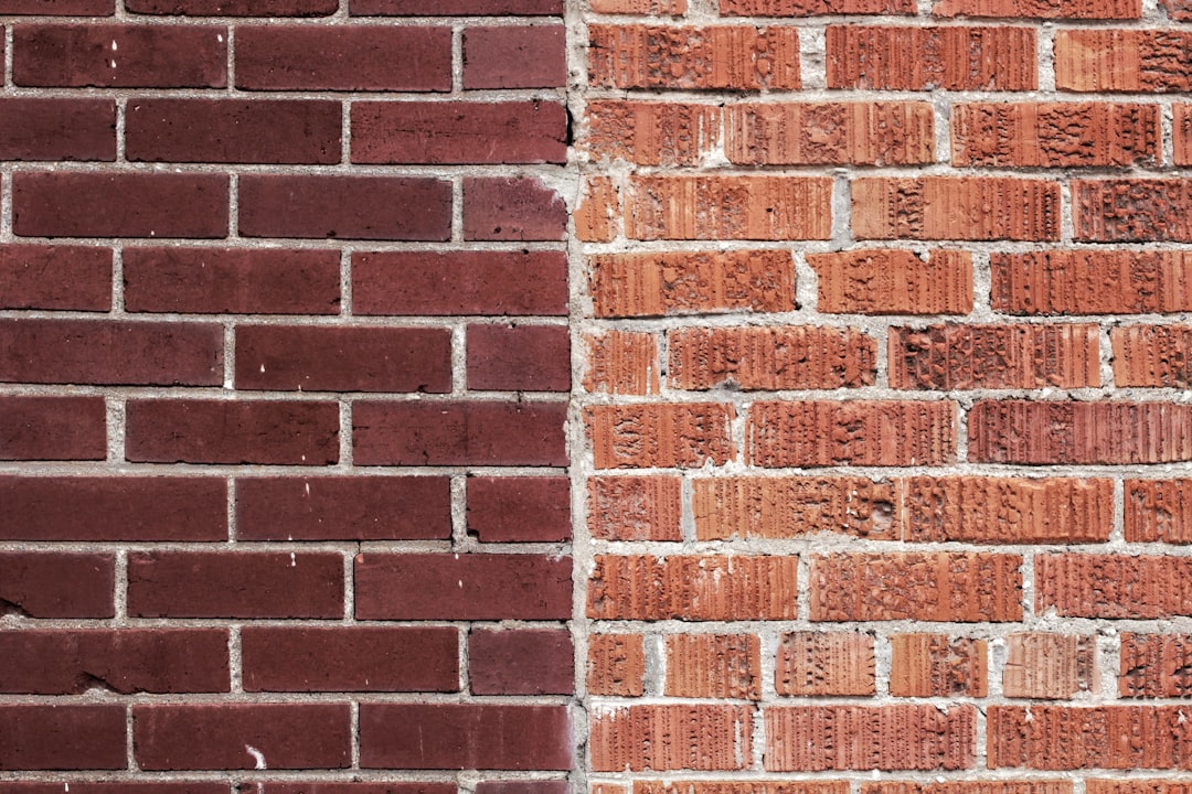 A red brick wall with half painted in dark brown color, contrasting the other side. The left part of it is painted and has a smooth texture while the right one shows the natural red brick pattern. It is a closeup photo focused on the texture and color contrast between the two parts. –ar 128:85