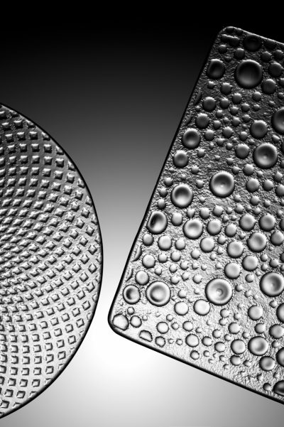 a close up of two different shaped glass textures, one rounded and the other is square with raised round dots on it, the background is black and white, monochromatic, dark gray gradient, texture, high contrast, hyper realistic, photography, studio light, high resolution photography, high definition, high detail, --ar 85:128