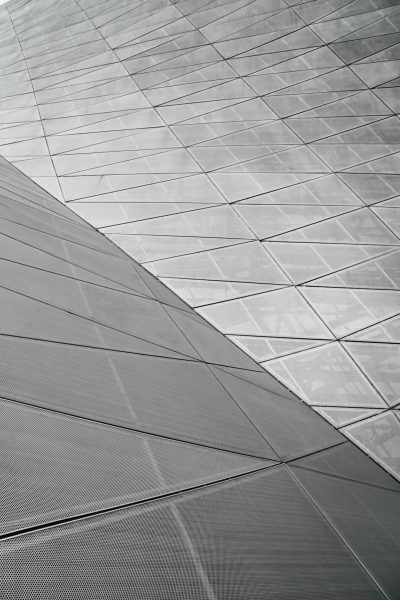 The roof of the museum building is made from triangular metal panels with an anodized surface, arranged in lines and curves. The camera angle shows closeup details of each panel. It is gray and white. --ar 85:128