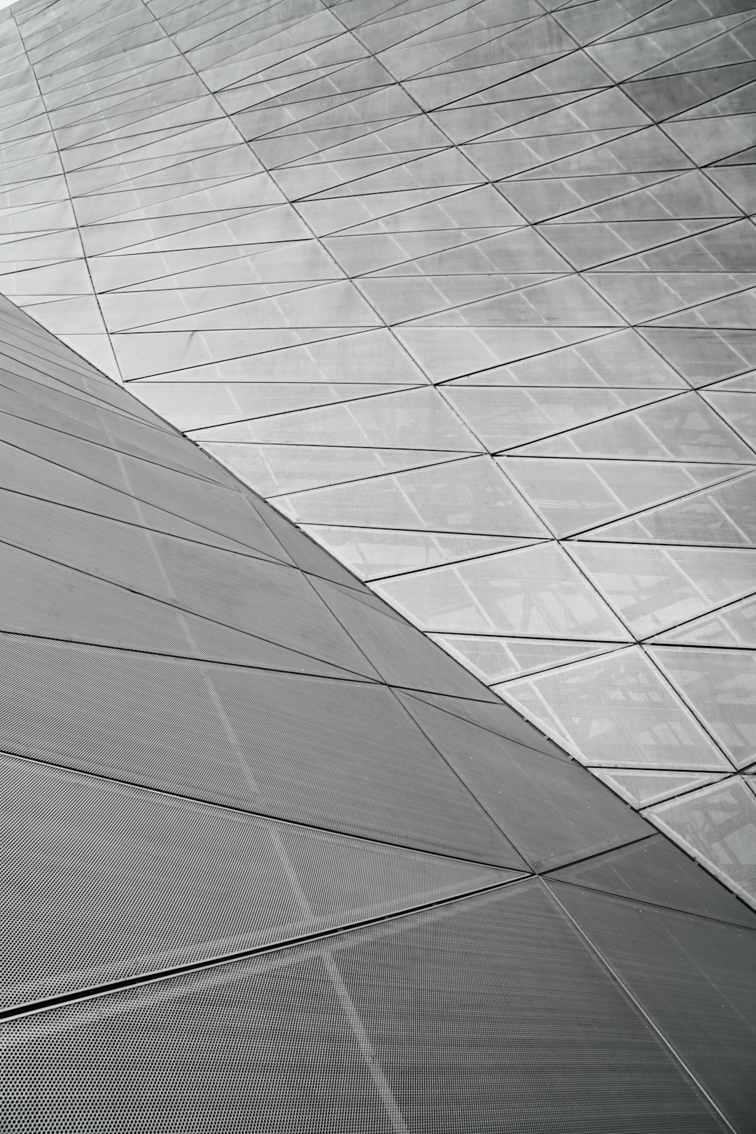 The roof of the museum building is made from triangular metal panels with an anodized surface, arranged in lines and curves. The camera angle shows closeup details of each panel. It is gray and white. –ar 85:128