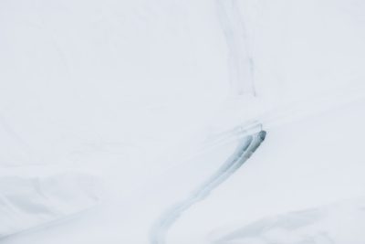 A snow-covered ground with an object covered in white powder, creating a long curved line on the surface of fresh snow, viewed from above. The background is pure white and minimalist. Captured using a Canon EOS R5 mirrorless camera with natural light. The scene conveys tranquility and minimalism in the style of a minimalist painter. --ar 128:85