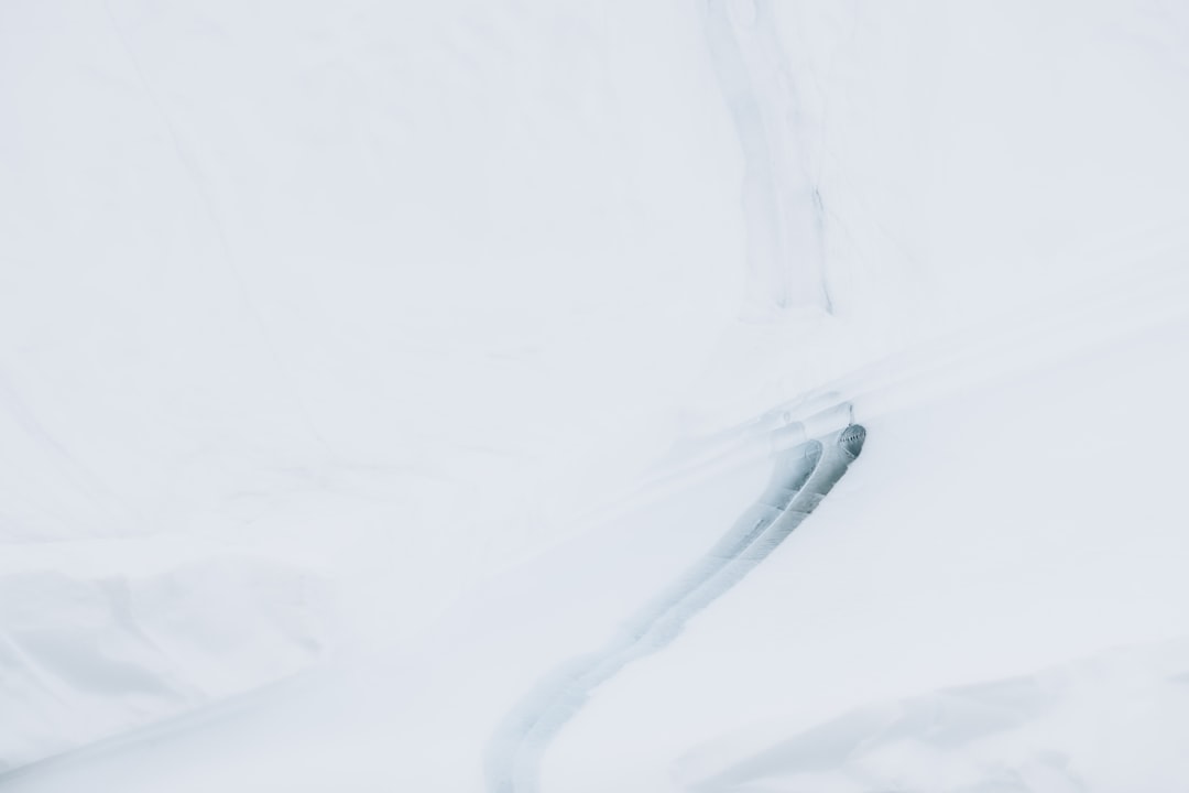 A snow-covered ground with an object covered in white powder, creating a long curved line on the surface of fresh snow, viewed from above. The background is pure white and minimalist. Captured using a Canon EOS R5 mirrorless camera with natural light. The scene conveys tranquility and minimalism in the style of a minimalist painter. –ar 128:85