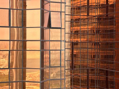 The peach and brown glass facade of a skyscraper, a Dubai cityscape view from a window, a building under construction, an industrial mesh structure, a warm sunset light. --ar 4:3