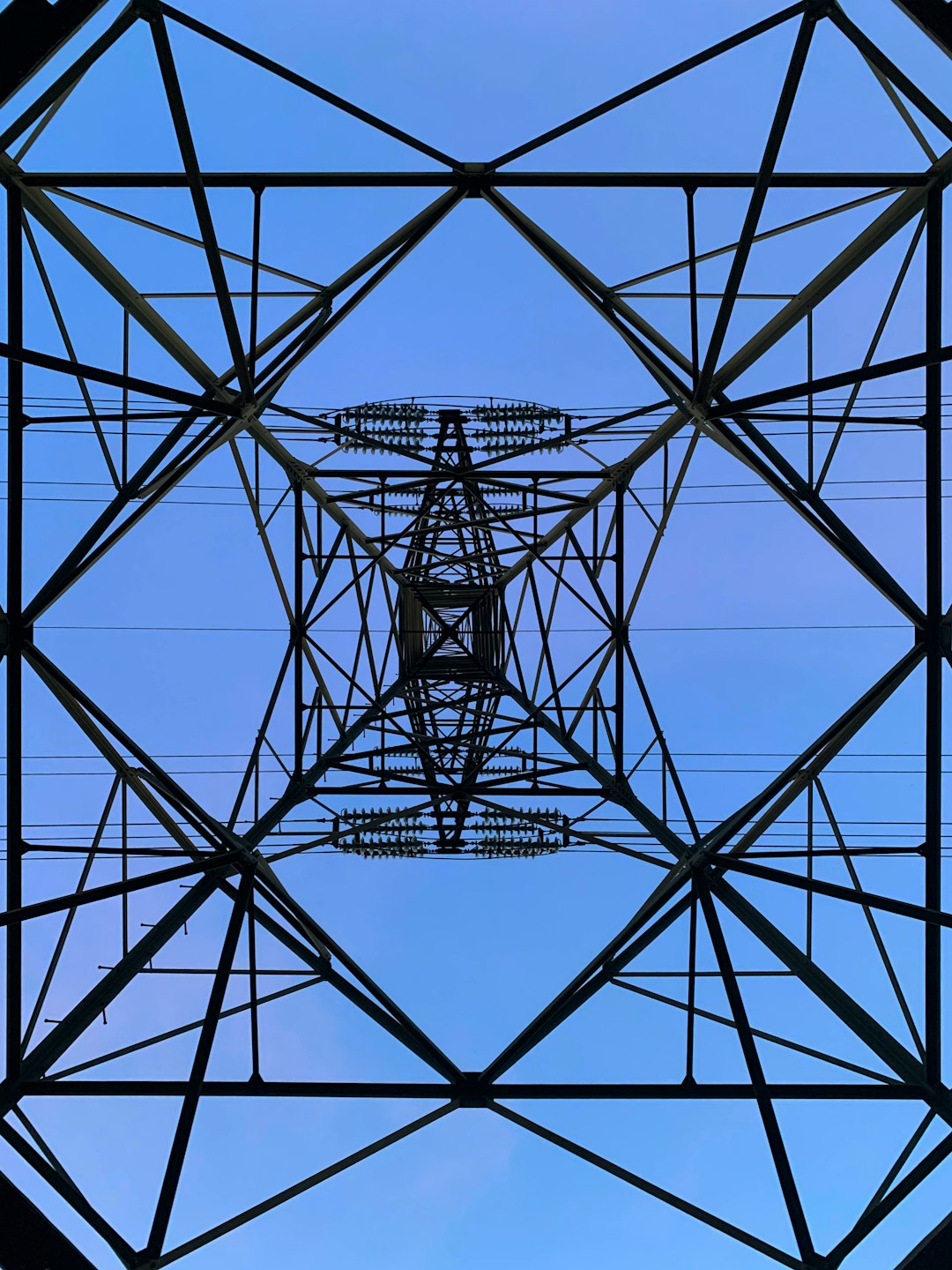 a symmetrical geometric pattern of an electric pammu tower, blue sky background, straight on camera view from the ground looking up at it, hyper realistic photography –ar 3:4