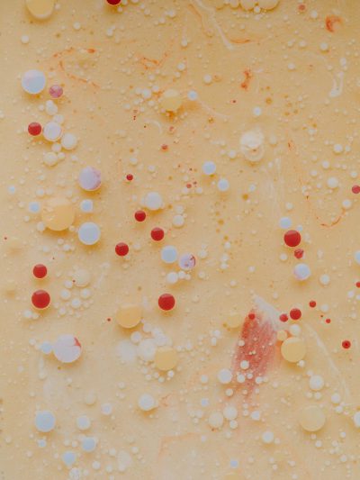 abstract painting of creamy yellow, cream cheese and red dots, with tiny drops of color floating in the liquid, macro photography, closeup, top view, low angle, soft lighting, high resolution, intricate details, hyperrealistic, highly detailed, macro lens, studio lighting, professional photograph, warm tones, texture, depth of field. --ar 3:4