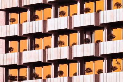 An apartment building with balconies and plants in the windows, symmetrical composition, light orange background, close up, photography in the style of [Wes Anderson](https://goo.gl/search?artist%20Wes%20Anderson). --ar 128:85