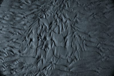 Dark grey sand texture with visible patterns of ripples and swirls, top view, high resolution photography, insanely detailed --ar 128:85