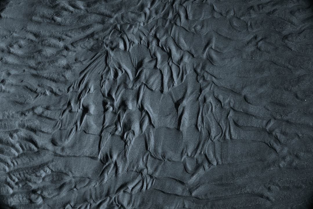 Dark grey sand texture with visible patterns of ripples and swirls, top view, high resolution photography, insanely detailed –ar 128:85