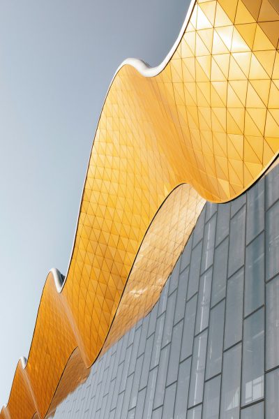 A building facade with yellow metal tiles and golden wave shaped pattern, featuring fluid lines, modern architecture, high resolution photography, and an exterior shot of the entire structure. The photo was taken in the style of [Iwan Baan](https://goo.gl/search?artist%20Iwan%20Baan) using a Canon EOS R5 camera. --ar 85:128