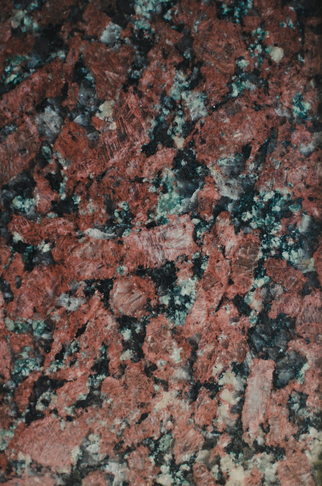 A closeup of red black granite with green and white veins, showcasing the intricate patterns in high detail. The background is a solid color to highlight the stone’s texture. This photograph was taken in the style of professional photographers using advanced techniques for highly detailed and sharp images. –ar 21:32