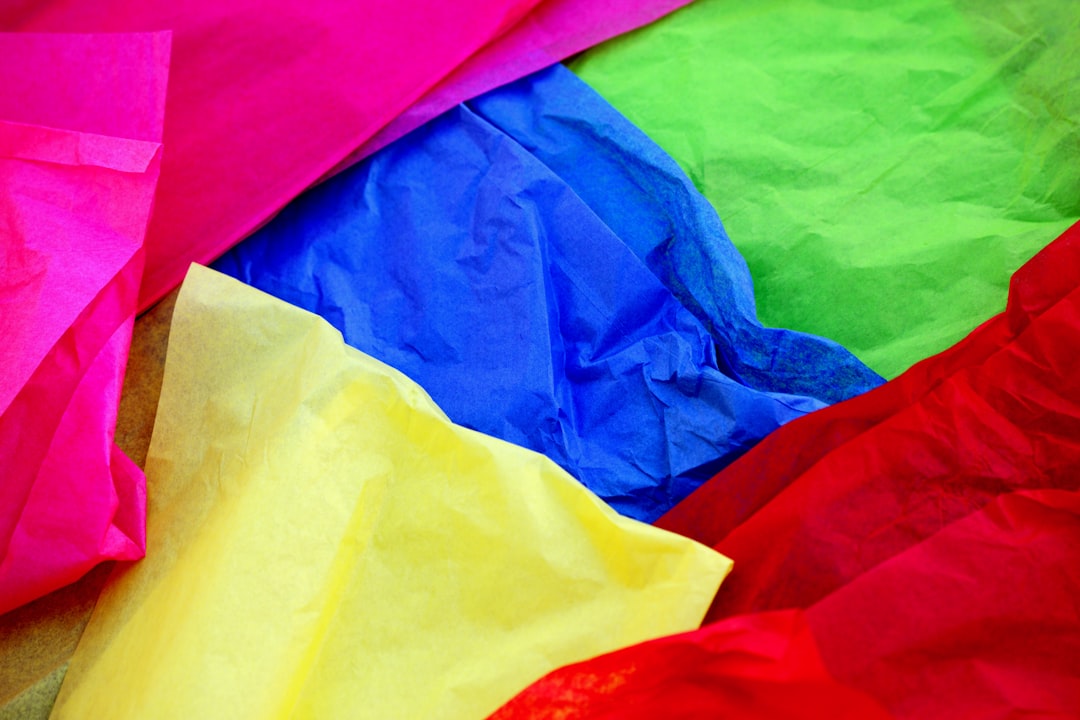 Closeup of colorful tissue paper in red, yellow, green, blue, pink and purple colors. The tissue paper is cut and arranged in the style of an abstract collage. –ar 128:85