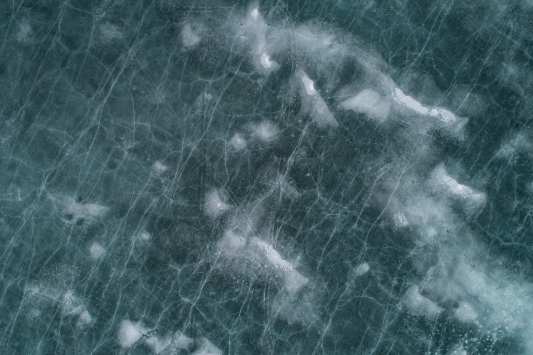 Top down view of ice with cracks and grooves, texture, in the style of photorealistic, in the style of hyperrealism, dark teal and white, in the style of photography. –ar 128:85