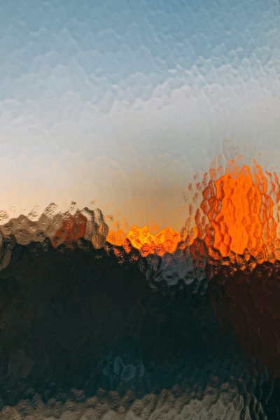 abstract image of sunset over the moutains, blurry, low quality, grainy, orange and blue colors, out focus, photo realistic, textured glass with water droplets on it, blurred foreground --ar 85:128