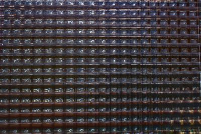 Closeup of the metal grid with multiple rows and columns, each row filled with numerous glass bottle bulbs in dark brown color. The background is blurred to emphasize details on texture, creating an abstract composition with a sense of depth. This artwork could symbolize urban life or cityscape, focusing on pattern and form. This photo was taken in the style of Canon EOS A20 camera. --ar 128:85