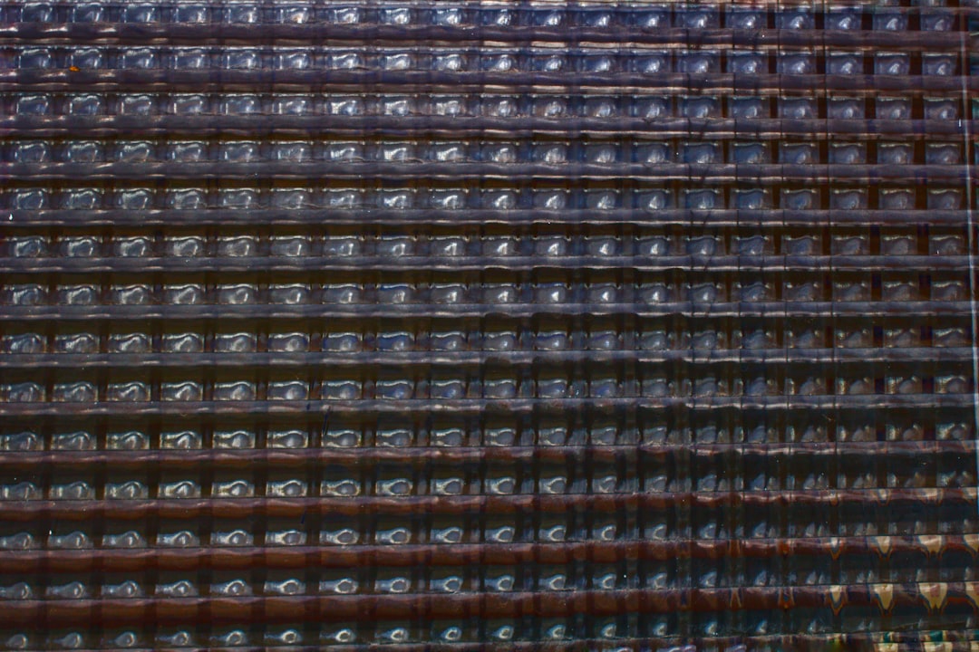 Closeup of the metal grid with multiple rows and columns, each row filled with numerous glass bottle bulbs in dark brown color. The background is blurred to emphasize details on texture, creating an abstract composition with a sense of depth. This artwork could symbolize urban life or cityscape, focusing on pattern and form. This photo was taken in the style of Canon EOS A20 camera. –ar 128:85