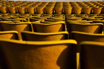 A photograph of yellow seats in an outdoor stadium, taken from the perspective of someone sitting on one chair looking at another row of chairs during golden hour with warm sunlight casting long shadows and highlighting each seat's texture and shape. The background is blurred to focus attention on the individual seating arrangement. Taken with a Canon EOS5D Mark III camera with macro lens, capturing intricate details of textures and colors in the style of Canon. --ar 128:85