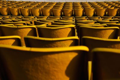 A photo of yellow seats in an outdoor stadium, seen from the front row. It has a symmetrical composition and was shot on Hasselblad medium format camera with a wide angle lens during the golden hour lighting. The photo shows intricate details.
