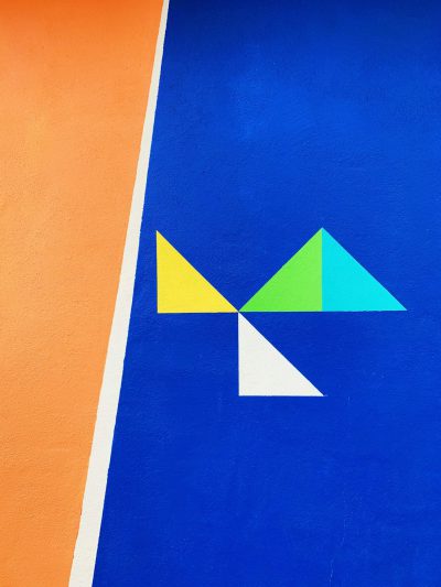 Colorful blue, orange and green wall with simple shapes, a white triangle in the middle of it, a yellow triangle in the top left corner and bottom right corner, an abstract shape made out of three different colors in the center of the picture, simple shapes, minimalistic style, high resolution. --ar 3:4