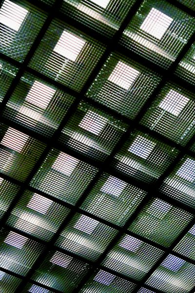 A photograph of the ceiling made from glass blocks, the glass is green and has grid patterns. The patterned light shines through the glass, creating shadows on the walls below. In sharp focus, the texture of each block is shown in detail. Taken with an iPhone camera, the image captures the intricate details of the glass blocks against the dark background, in the style of an iPhone camera. --ar 85:128