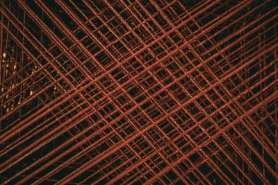 A pattern of rusted steel mesh with crosshatching, captured in high resolution. The red color adds contrast to the dark background and highlights intricate details like thin lines or dust particles on each wire frame. This texture is perfect for architectural and industrial design projects that look down from above in the style of looking down from above. --ar 128:85