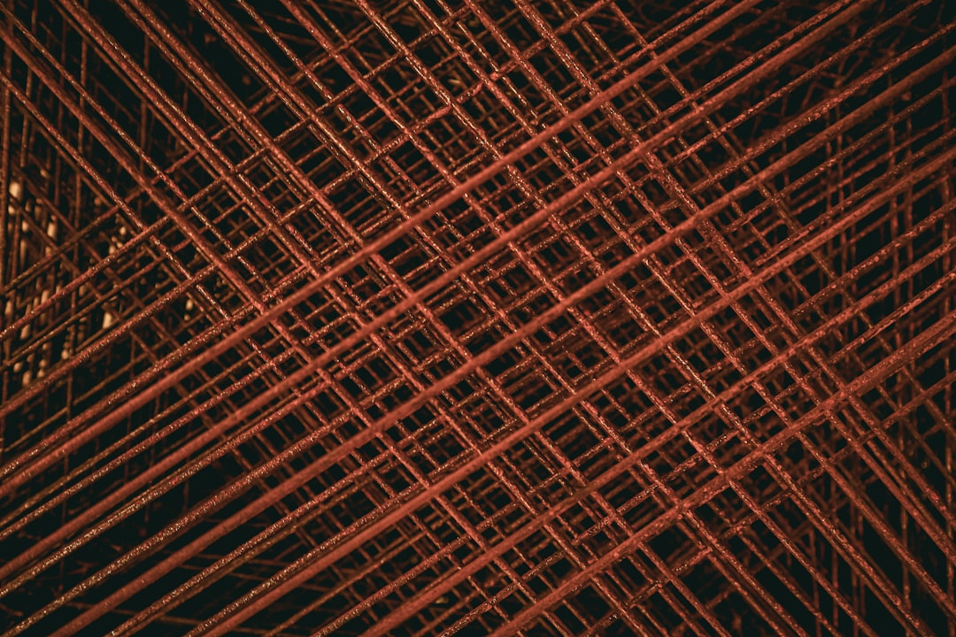 A pattern of rusted steel mesh with crosshatching, captured in high resolution. The red color adds contrast to the dark background and highlights intricate details like thin lines or dust particles on each wire frame. This texture is perfect for architectural and industrial design projects that look down from above in the style of looking down from above. –ar 128:85