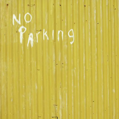 A yellow metal wall with the words "NO parking" written in white paint, front view, full shot, in the style of photography.