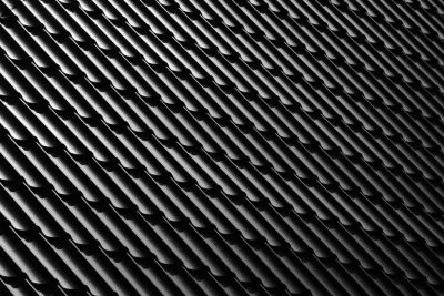 A high-resolution photograph of an industrial black metal roof with repeating vertical lines, showcasing the texture and depth in monochrome tones. The focus is on the contrast between sharp angles and soft edges, creating visual harmony within the patterned surface. The lighting highlights the metallic sheen and intricate details for potential commercial use. --ar 128:85