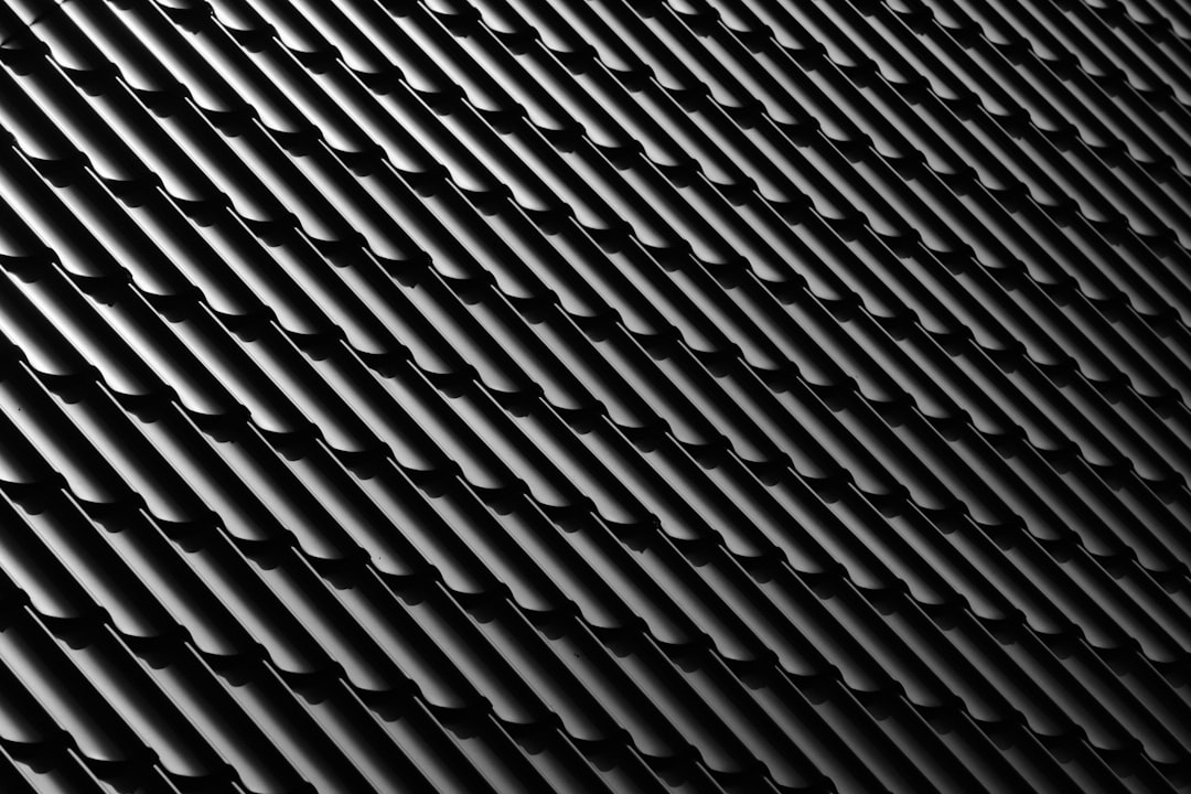 A high-resolution photograph of an industrial black metal roof with repeating vertical lines, showcasing the texture and depth in monochrome tones. The focus is on the contrast between sharp angles and soft edges, creating visual harmony within the patterned surface. The lighting highlights the metallic sheen and intricate details for potential commercial use. –ar 128:85